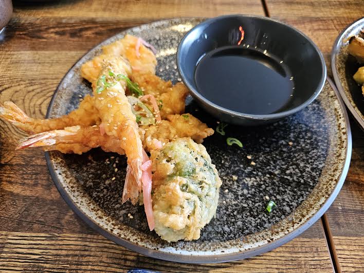 prawn tempura on a black round plate with a bowl of black sauce