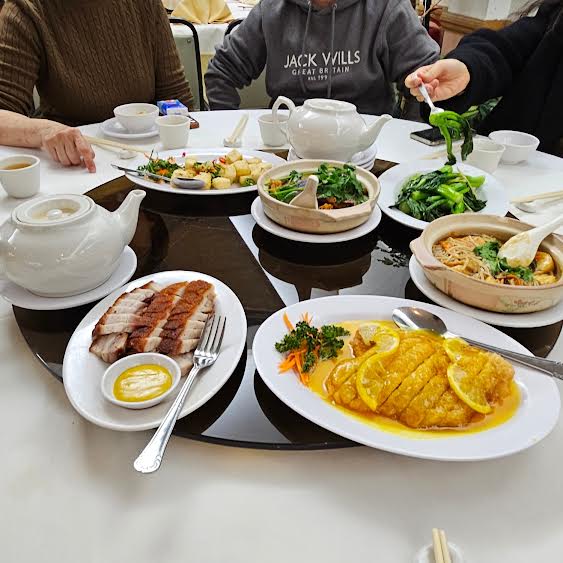 dishes on a lazy susan with 2 teapots: lemon chicken, green vegetables, roast crackling pork and tofu. 