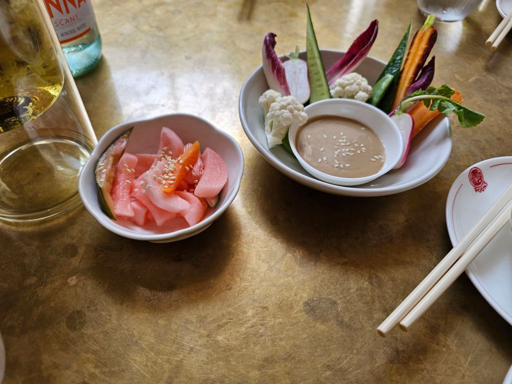 crudites with sesame dressing in a separate bowl with a dish of pickles alongside