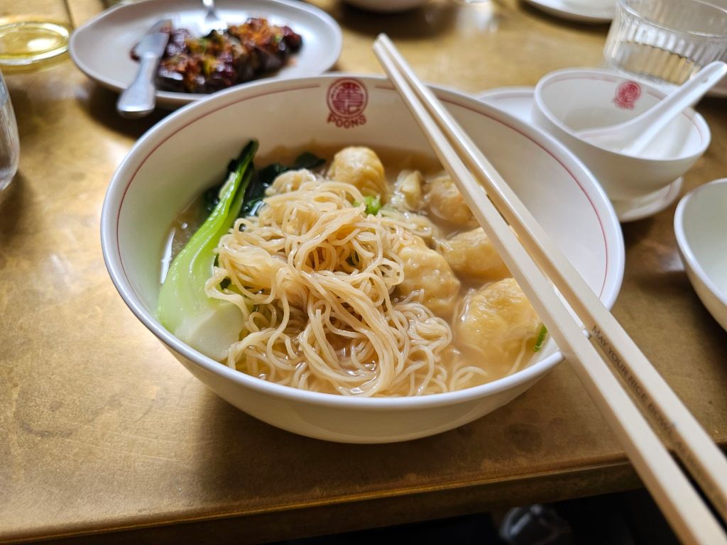 noodles in soup with green veg and wontons. A pair of chopsticks on top of bowl.